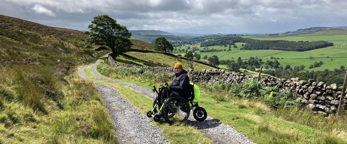 A main in a motorised wheelchair on a green lane in upland countryside