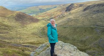 a woman standing on an upland path in the middle of a range of green hills