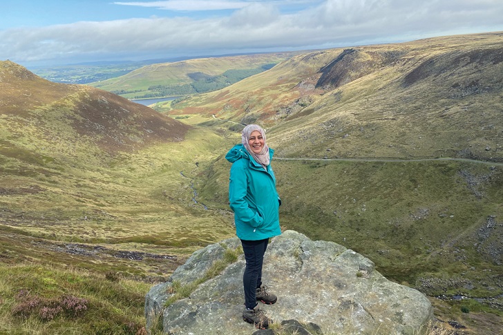 a woman standing on an upland path in the middle of a range of green hills