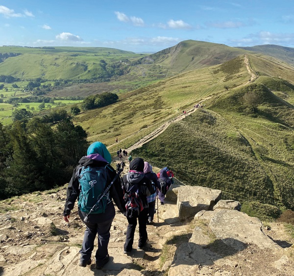 A group of women descending a steep path along a ridge of green hills