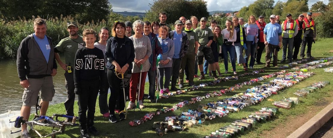 a group of litter pickers by a canal with collected rubbish on the ground in front of them