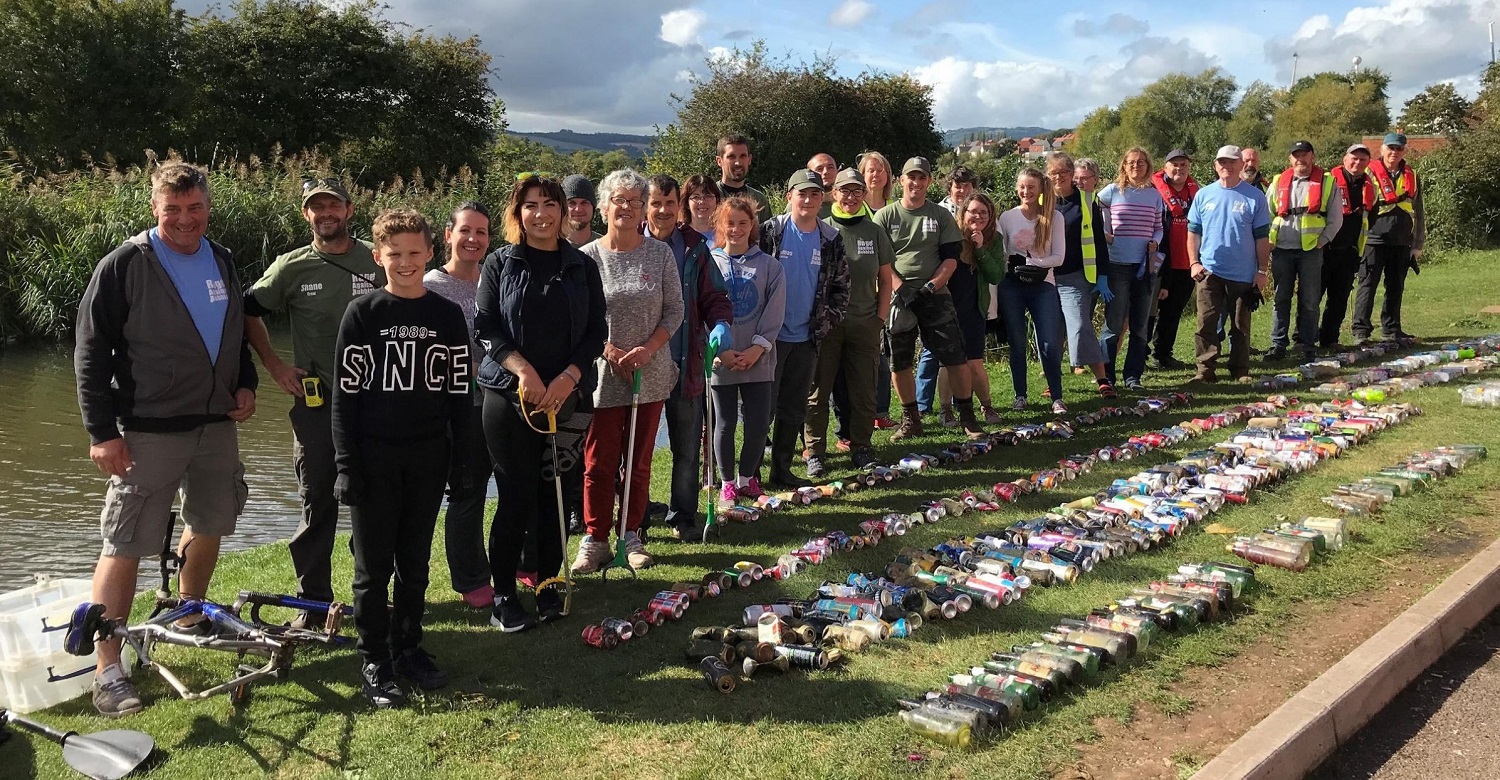 a group of litter pickers by a canal with collected rubbish on the ground in front of them