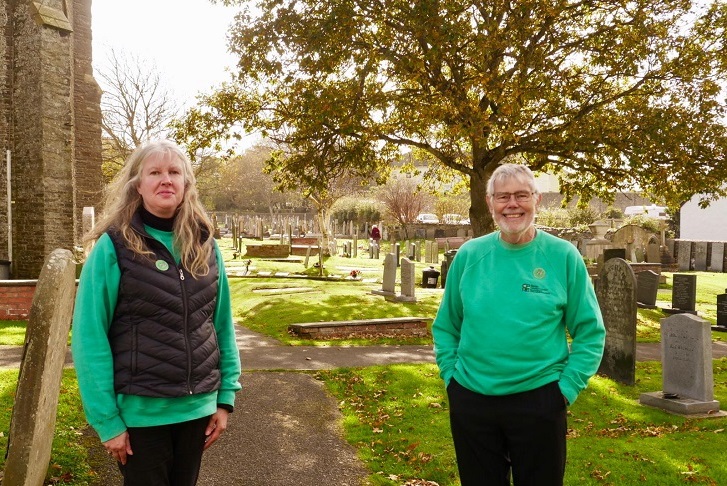 a man and woman standing in a churchyard with trees in autumn