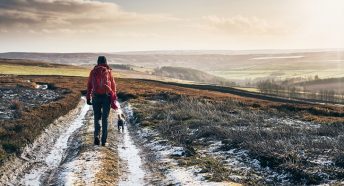 a woman walking a dog on frosty moorland with hills on the horizon
