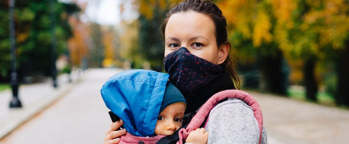 A woman wears a mask and holds a small child