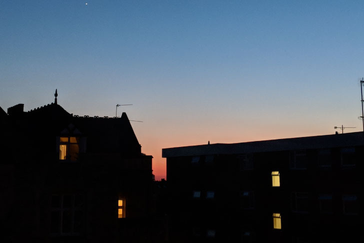 The pink glow of a sunrise behind some dark houses