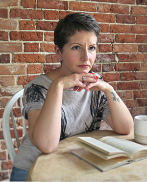A woman reading at a table in front of a brick wall