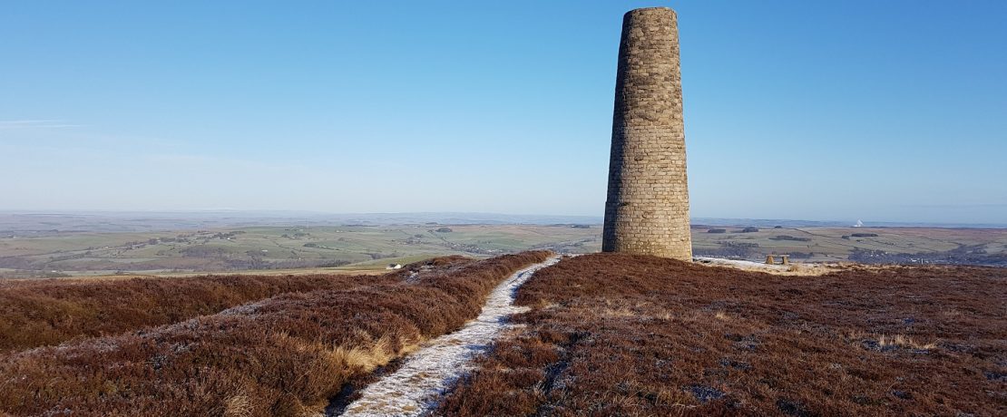 A frosty path towards a brick smelting chimney tower through upland moorland with a clear blue sky above