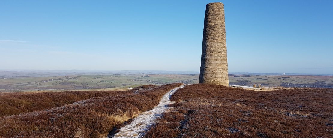 A frosty path towards a brick smelting chimney tower through upland moorland with a clear blue sky above