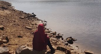Woman in headscarf sitting at edge of lake