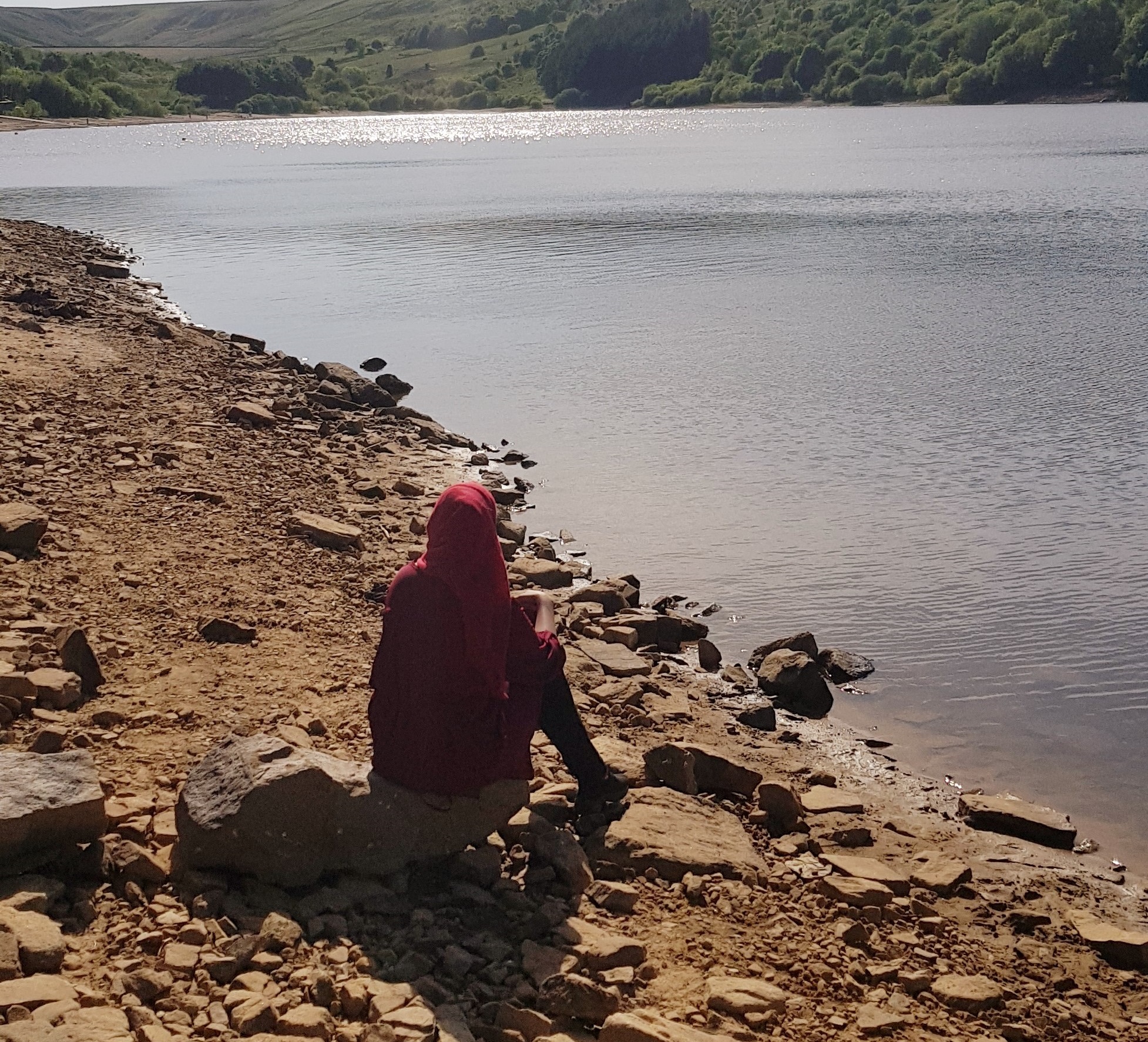 Woman in headscarf sitting at edge of lake