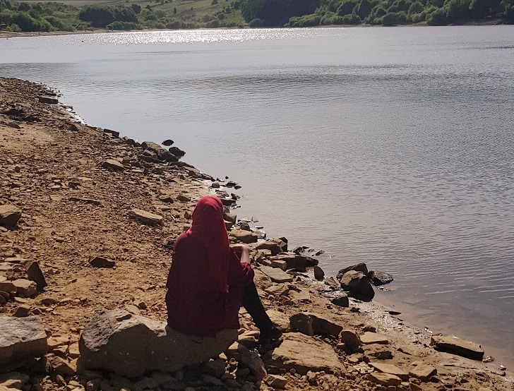 Woman in red headscarf sitting looking out at lake