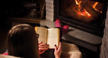 a woman reading a book in front of a fire