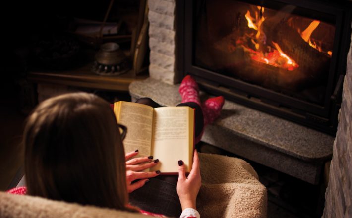 a woman reading a book in front of a fire