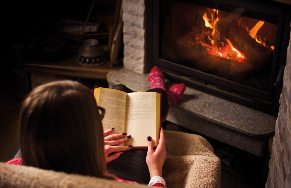 a woman reading a book in front of a fire