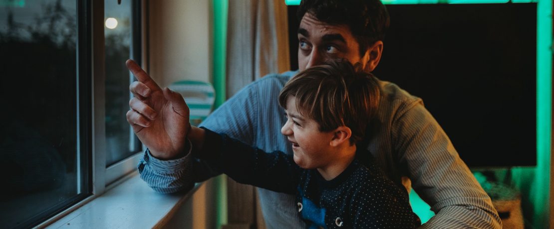 A father and son look out of a window from inside a house to a dark sky