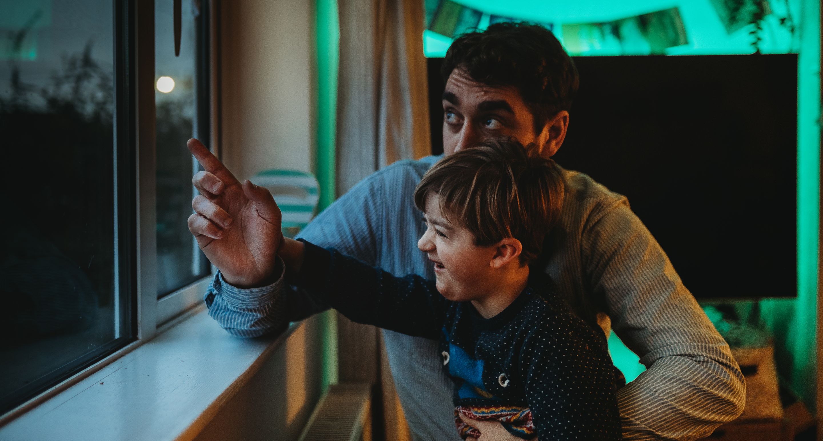 A father and son look out of a window from inside a house to a dark sky