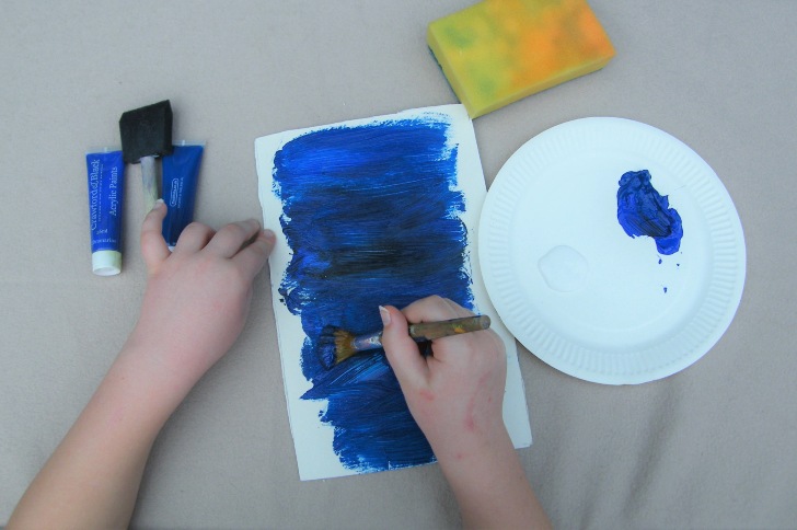 A child's hand painting blue paint onto card