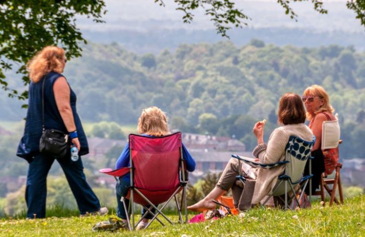 Four women picnic on a hill with woodland visible below