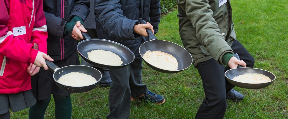 Four pans with pancakes held by separate arms of people ready to toss them