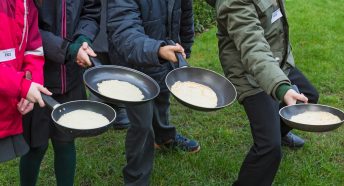 Four pans with pancakes held by separate arms of people ready to toss them