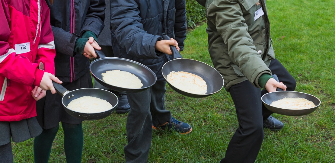 Four pans with pancakes held by separate arms of people ready to toss them