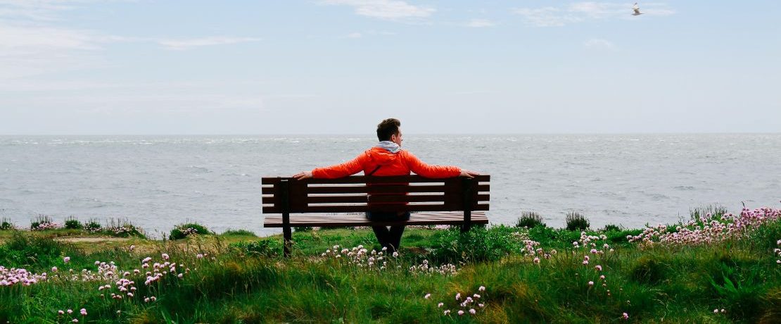 Man sitting by the coast on a bench