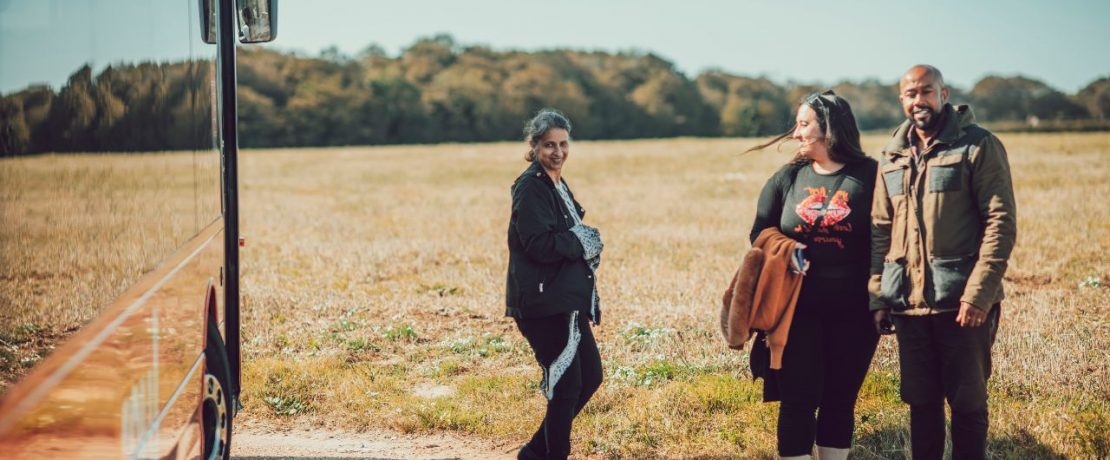 Three people standing beside a bus parked by a field