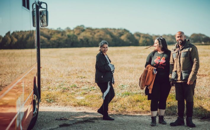 Three people standing beside a bus parked by a field