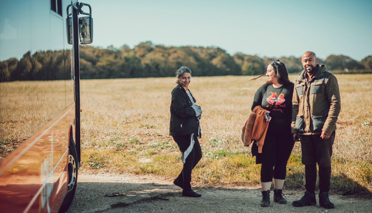 Three people standing beside a bus parked by a field