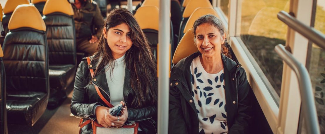 Two women sit on a rural bus service and face the camera