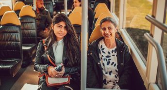 Two women sit on a rural bus service and face the camera