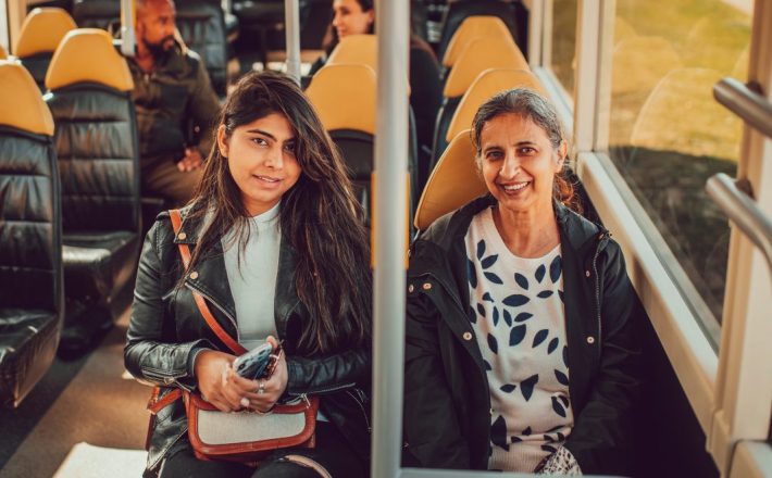 Two women sit on a rural bus service and face the camera