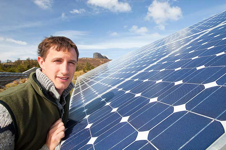 A man stands close to a solar panel on a sunny day