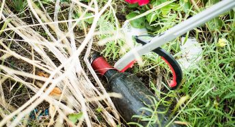 A discarded beer bottle in grass being picked up by a litter pincer