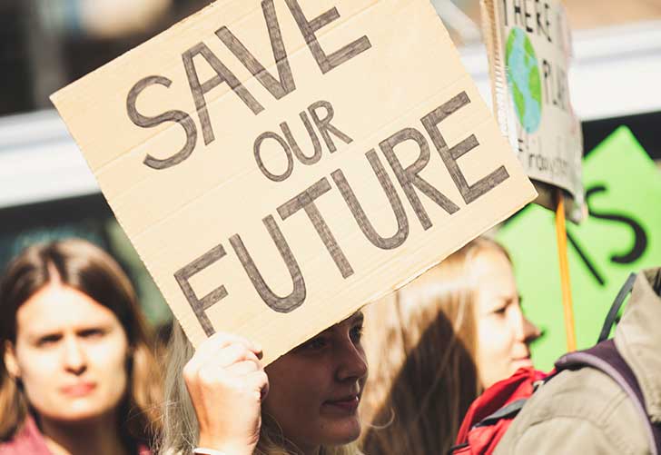 A young woman in a crowd holds a cardboard sign saying 'Save our future;