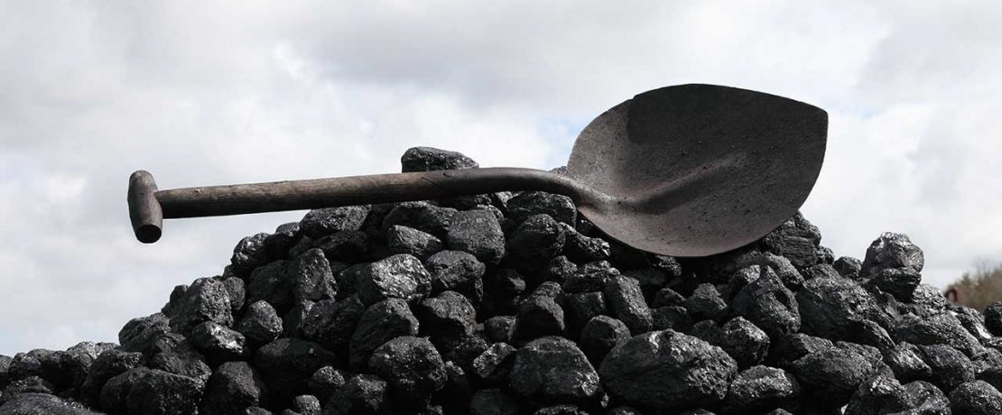 A pile of black coal with a dark metal shovel balanced on top