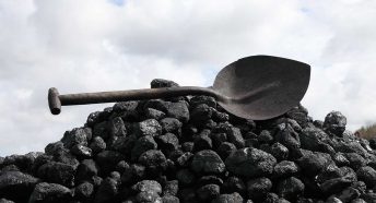 A pile of black coal with a dark metal shovel balanced on top