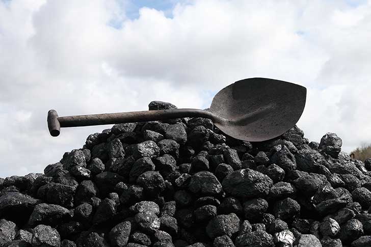 A pile of black coal with a dark metal shovel balanced on top