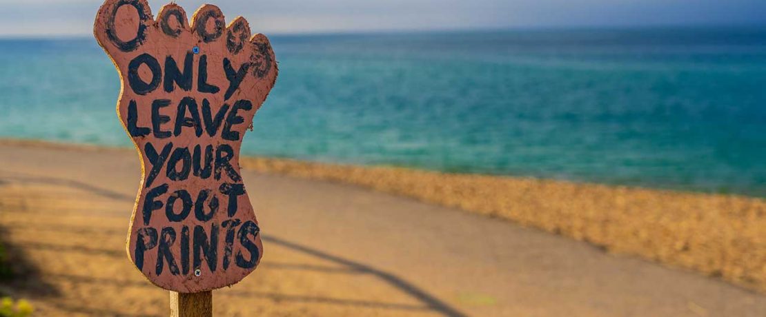 A footprint-shaped sign saying 'only leave your footprints' by a beach