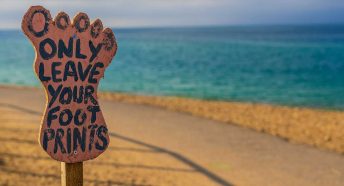 A footprint-shaped sign saying 'only leave your footprints' by a beach