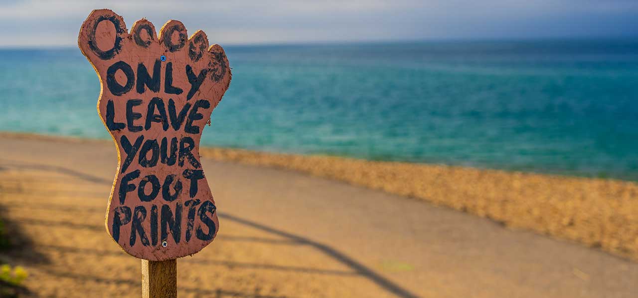 A footprint-shaped sign saying 'only leave your footprints' by a beach