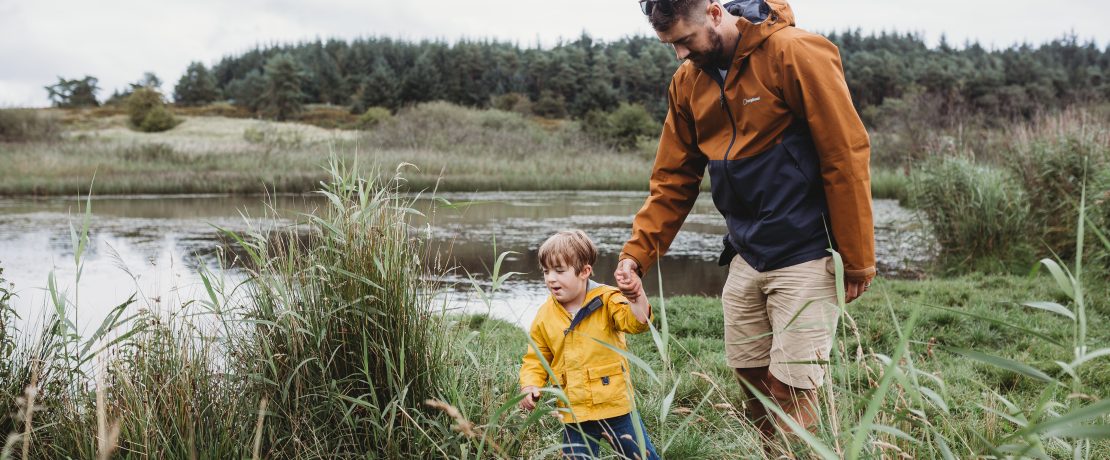 Father and young son walking in long grass by large fresh body of water