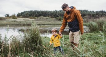 Father and young son walking in long grass by large fresh body of water