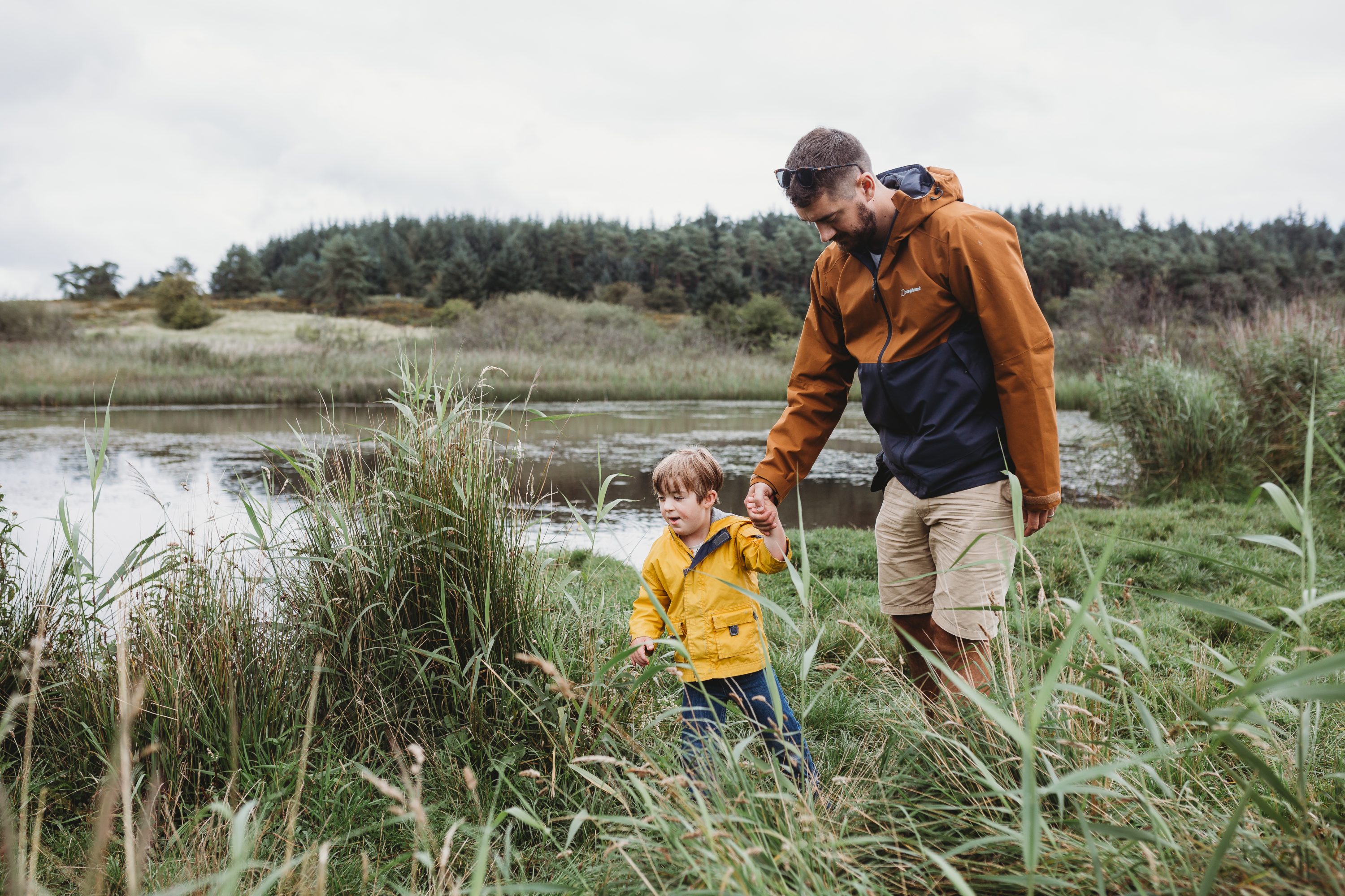 Father and young son walking in long grass by large fresh body of water