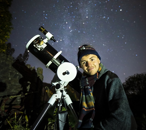 A man with a telescope in front of a star-filled sky