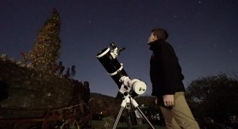 A man and telescope in a garden under starry skies