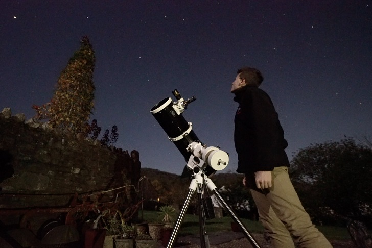 A man and telescope in a garden under starry skies