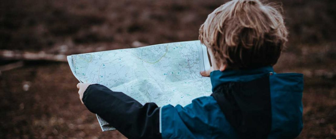 A small boy holds up a map with the countryside visible behind