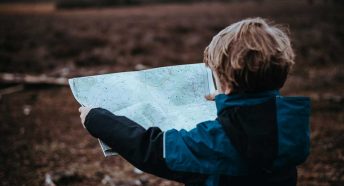 A small boy holds up a map with the countryside visible behind